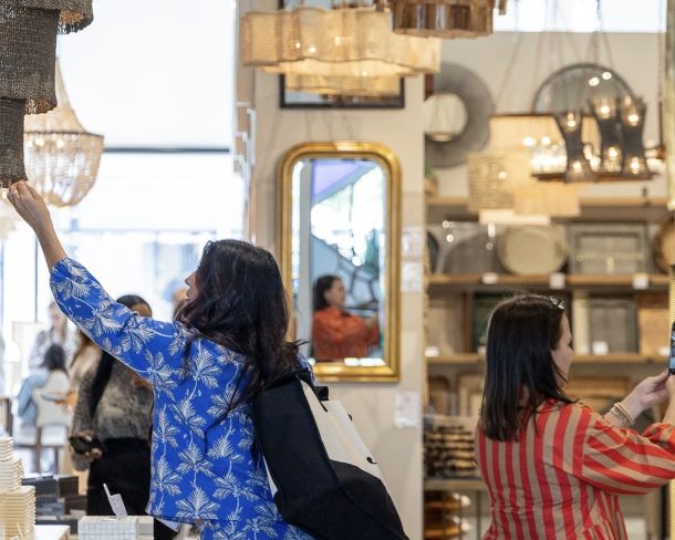 A bustling crowd walks throughout a design market in sunny north carolina, passing a large, colorful display of design advertisements and furniture layouts.