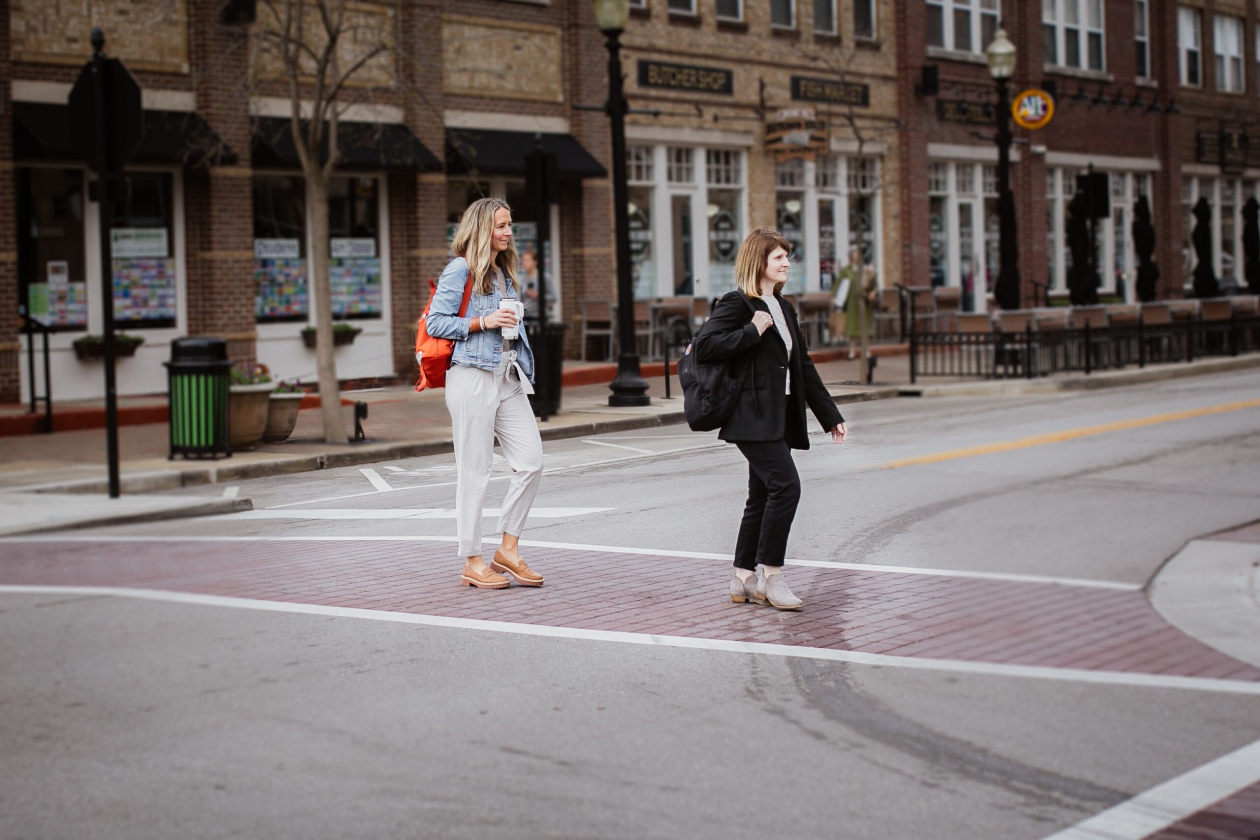 Two women cross the street near a building, enjoying a casual work outing together.