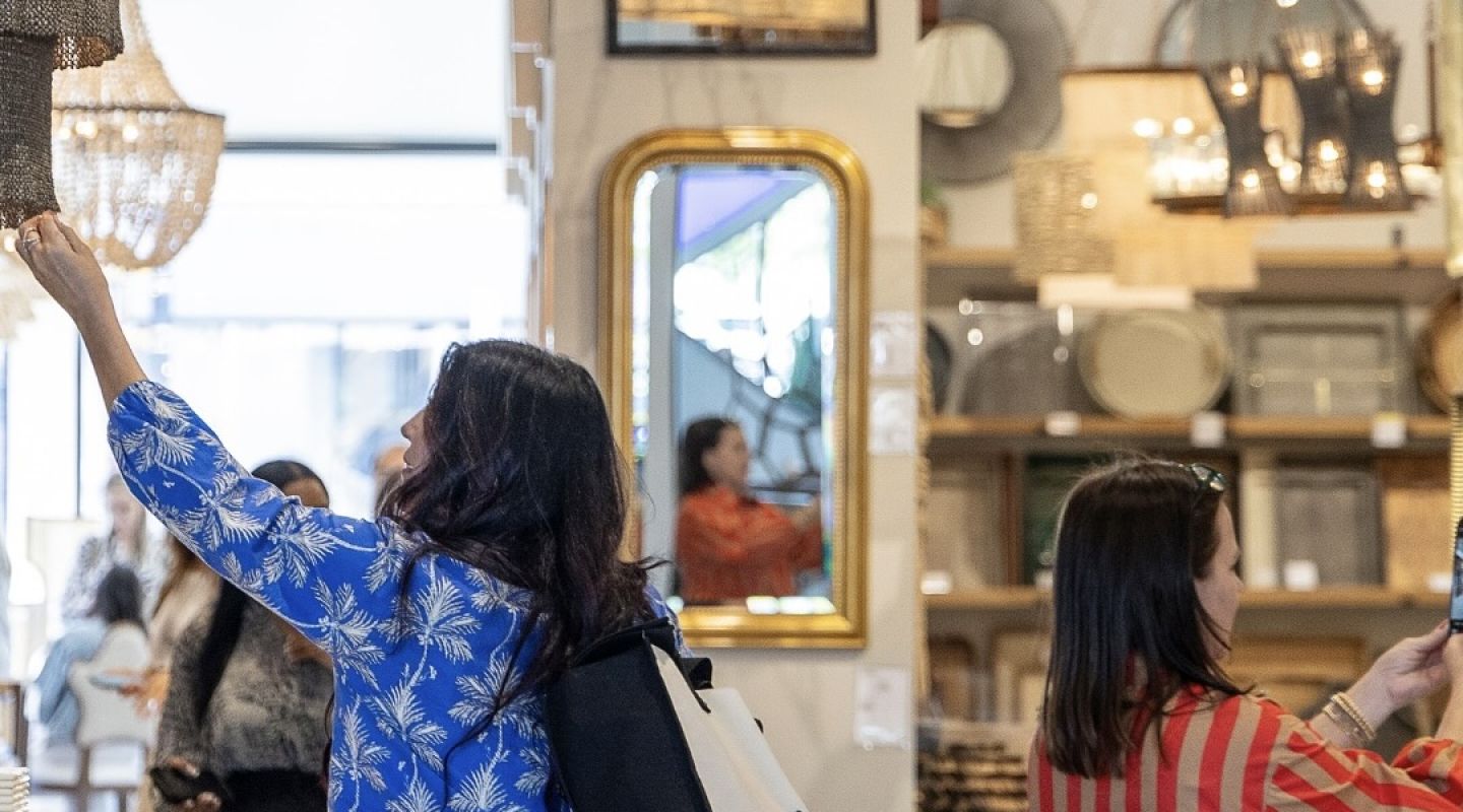 A bustling crowd walks throughout a design market in sunny north carolina, passing a large, colorful display of design advertisements and furniture layouts.