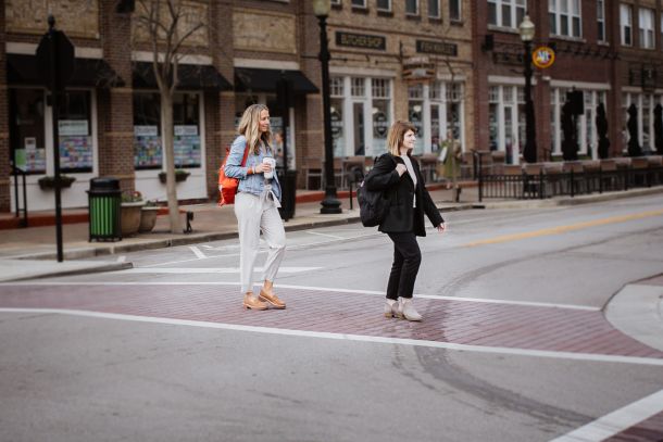 Two women cross the street near a building, enjoying a casual work outing together.