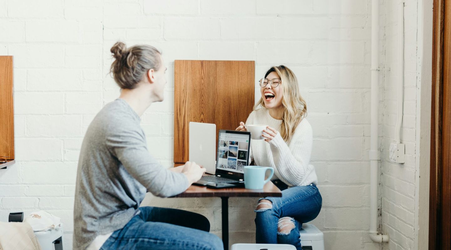 A man and woman sharing coffee and working on their laptops