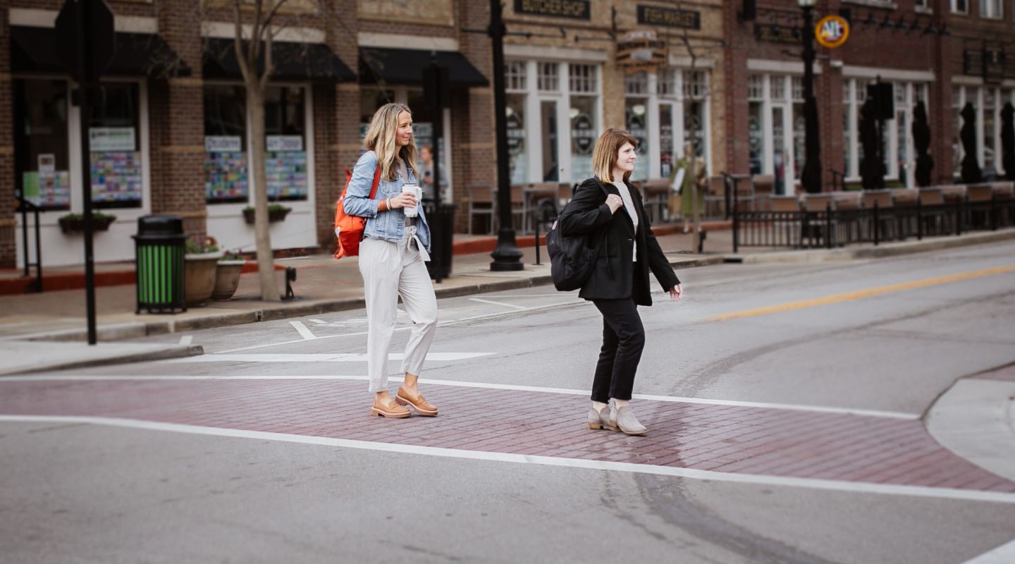 Two women cross the street near a building, enjoying a casual work outing together.